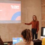 Delavnica o informacijski pismenosti. Predavateljica stoji pred skupino oseb, ki jo zavzeto poslušajo.
