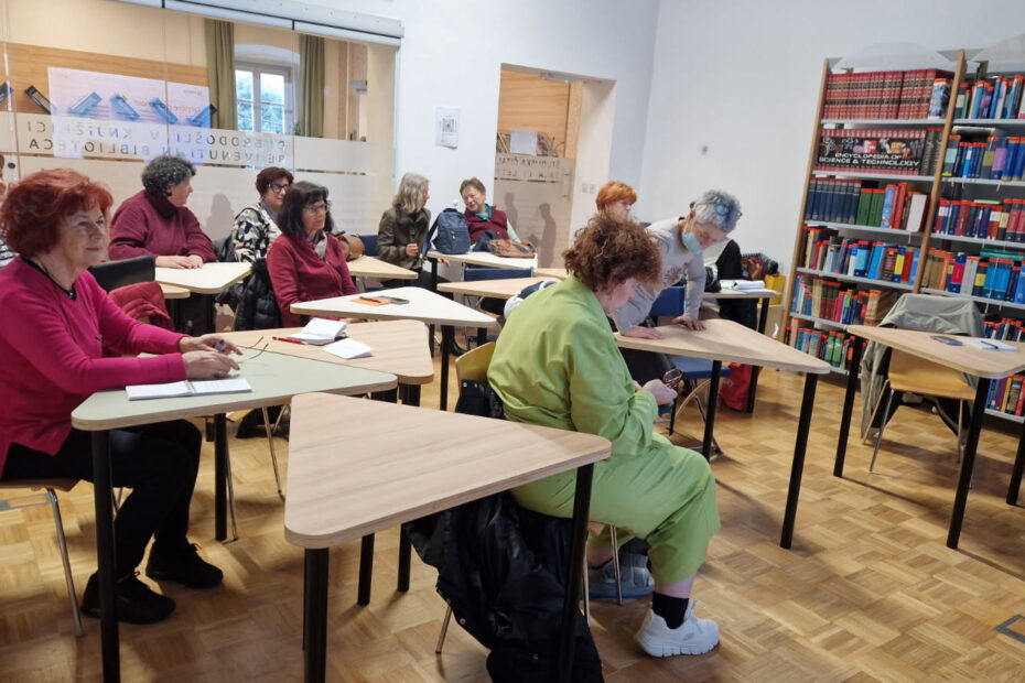 Člani društva UNI3 sedijo za mize in pripravljajo zapiske za delavnico o elektronskih virih